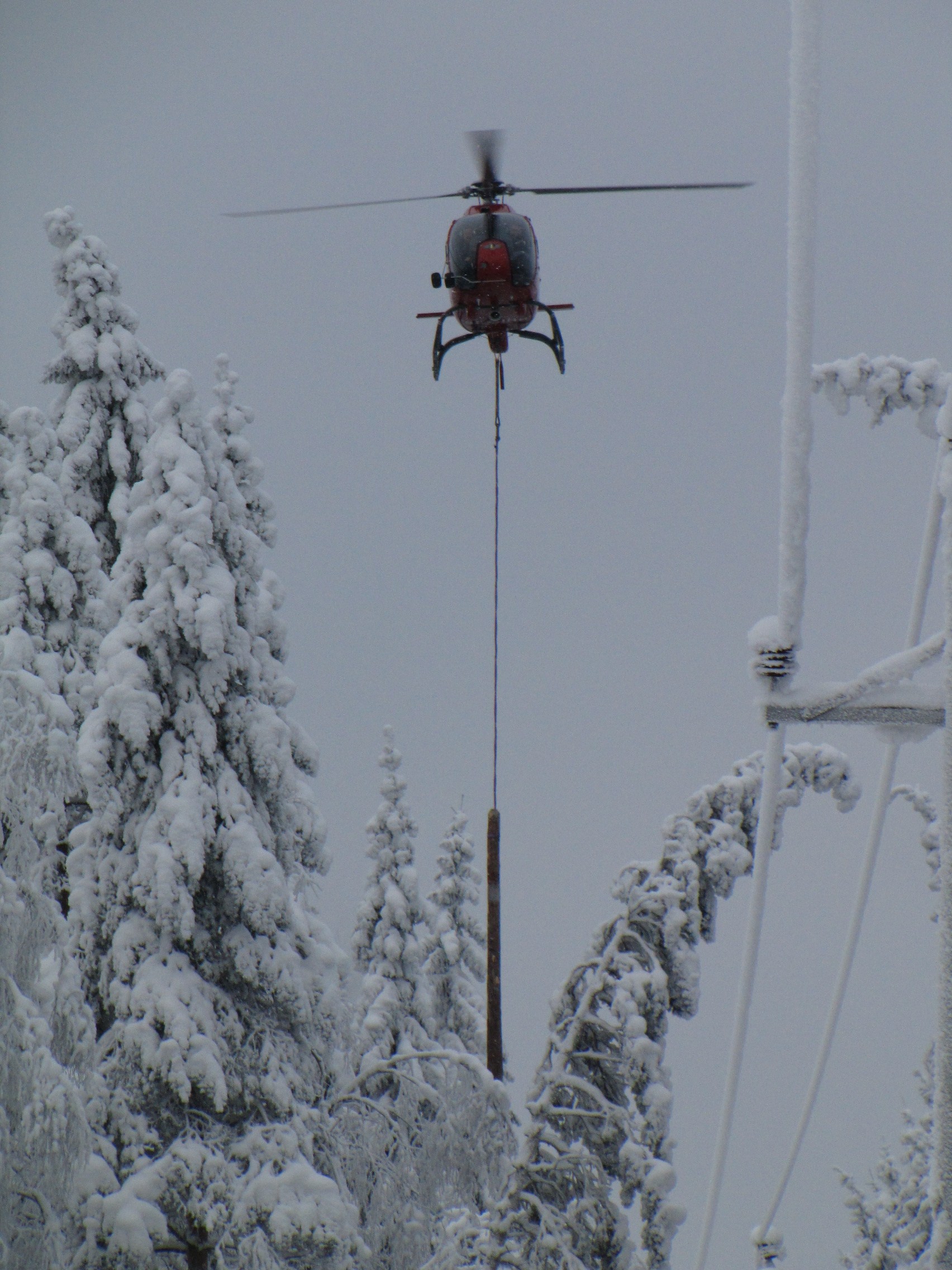A helicopter is a great help in detecting, preventing and repairing the damage caused to power lines by snow load. It may take a long time to find a tree that has bent across or fallen down on a power line deep in the forest, unless you use a helicopter. They are also used to map areas with risk of snow load, and information on this can be sent to the maps of repair teams via the mobile network. The photo shows snow being dropped with the help of a helicopter pulling a short log attached to a wire rope along the edge of the power line corridor. The log hits the trees bent across the corridor and causes the snow to fall off. For the pilot, this is an extremely demanding task, as the log must be prevented from touching the power lines at all times. Photo: Elenia